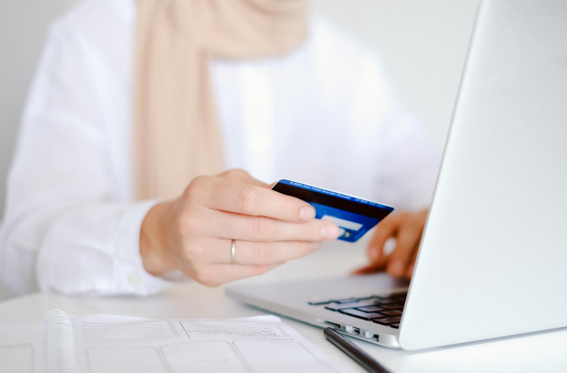 Dłoń z kartą kredytową przed laptopem podczas zakupów online