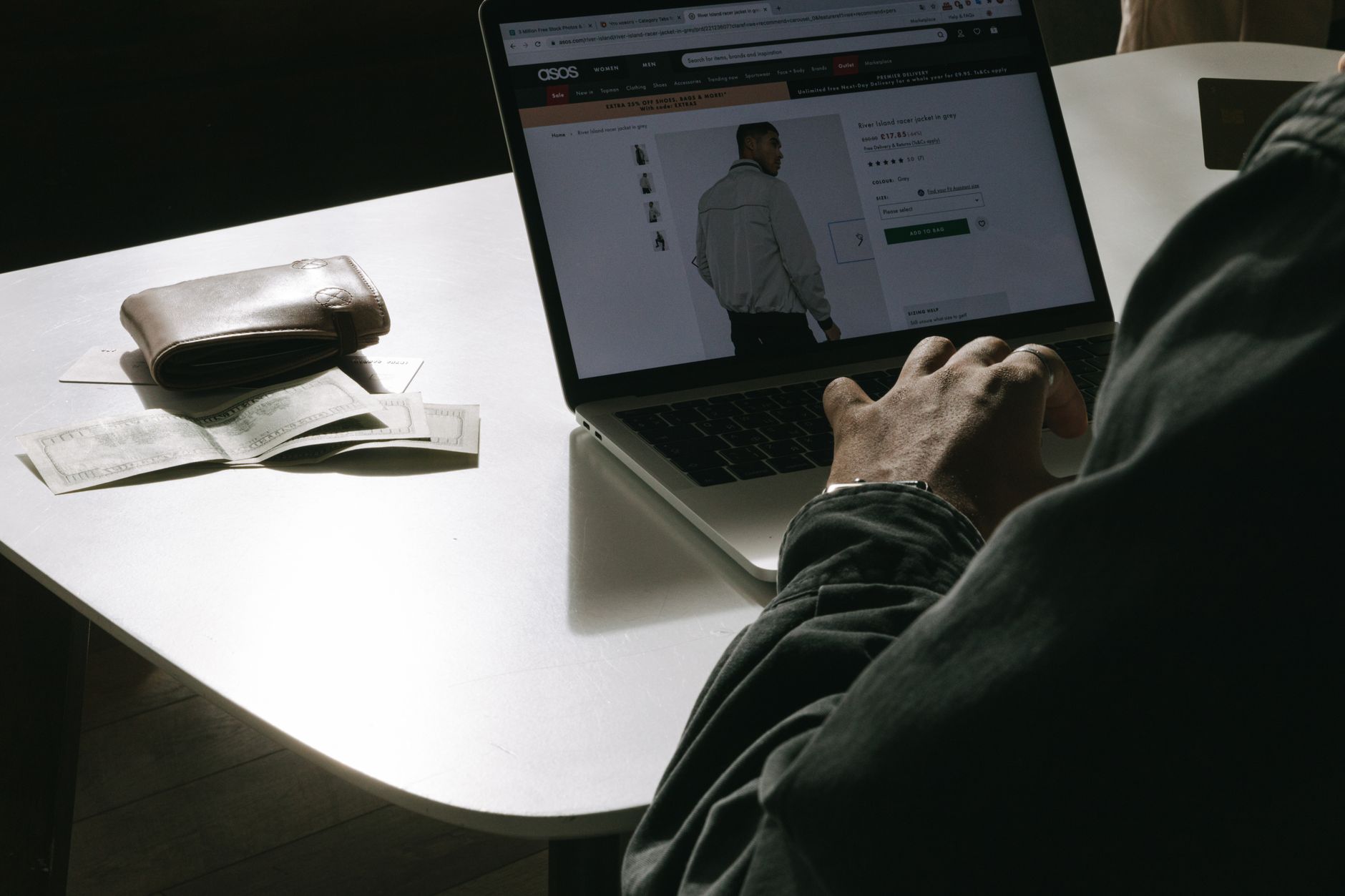 Mężczyzna w domu kupuje ubrania online na laptopie, obok leży portfel