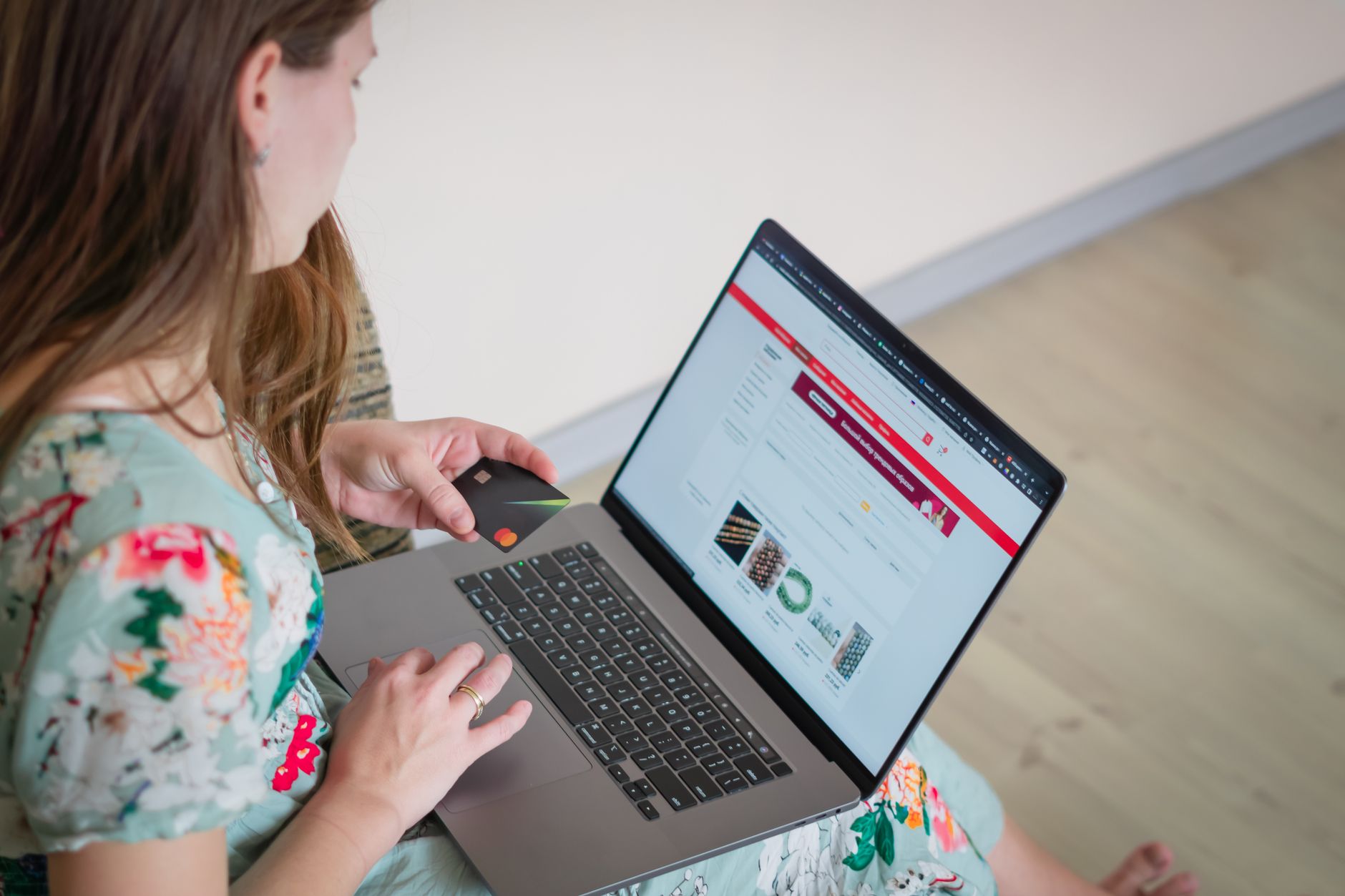 Kobieta w kwiecistej sukience robi zakupy online kartą przy laptopie