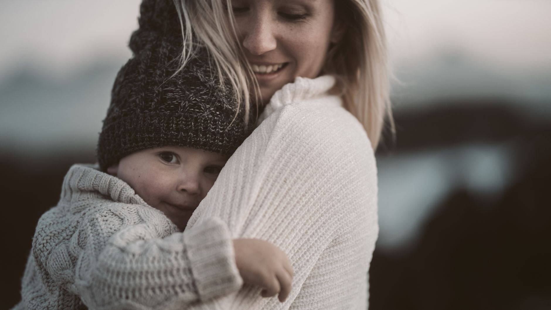 Mama przytula dziecko na zewnątrz, oboje w ciepłych swetrach